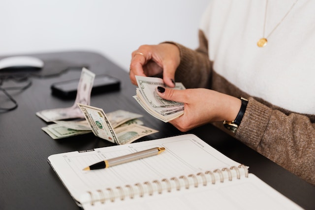 person in a white and brown sweater counting cash while sitting at their desk